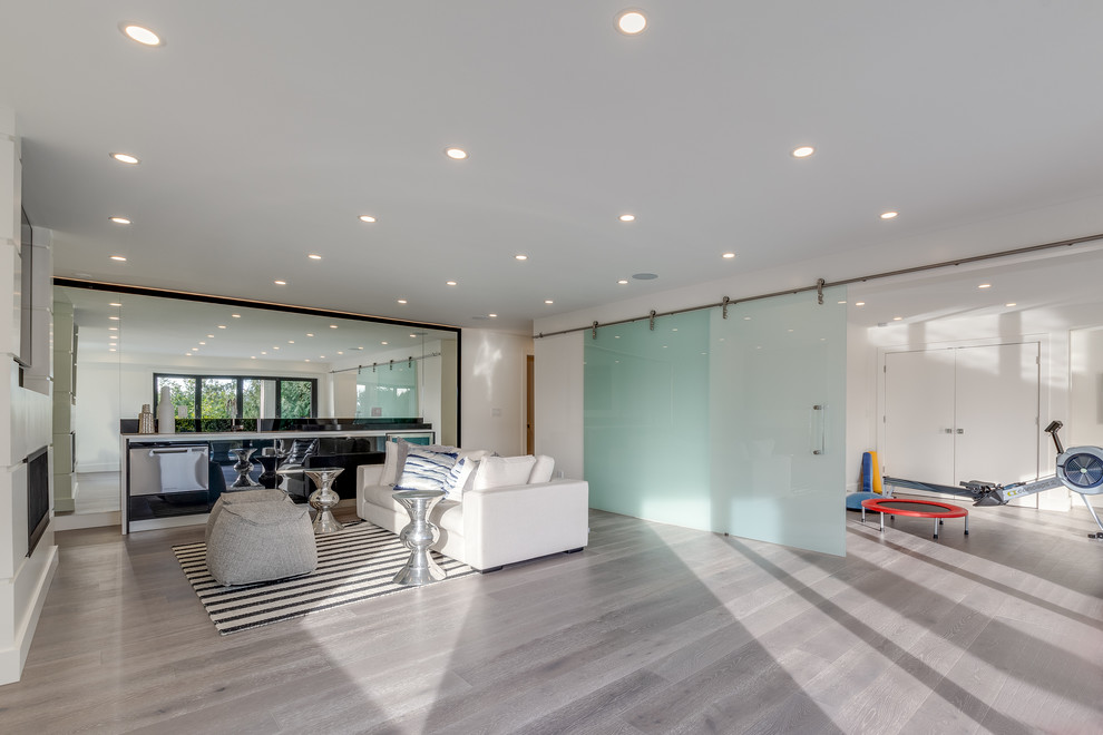 This is an example of a medium sized modern open plan games room in Vancouver with white walls, light hardwood flooring, a ribbon fireplace, a plastered fireplace surround, a built-in media unit and grey floors.