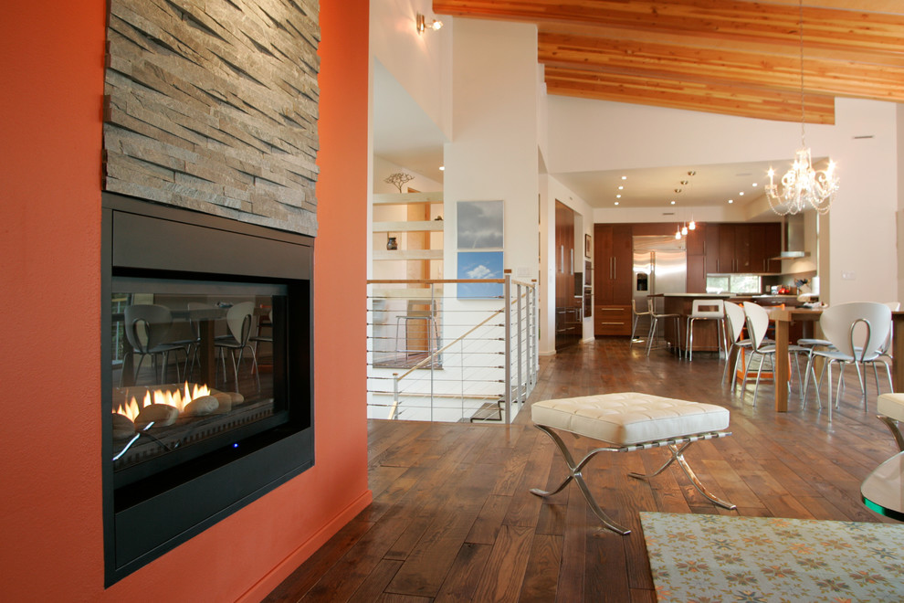 Inspiration pour une grande salle de séjour design ouverte avec un mur orange, un sol en bois brun, une cheminée standard, un manteau de cheminée en pierre et aucun téléviseur.