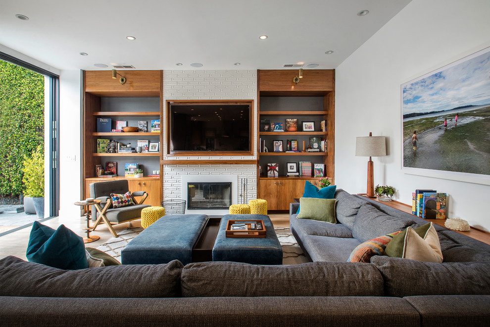 На фото: гостиная комната в стиле неоклассика (современная классика) с белыми стенами, стандартным камином, телевизором на стене и с книжными шкафами и полками