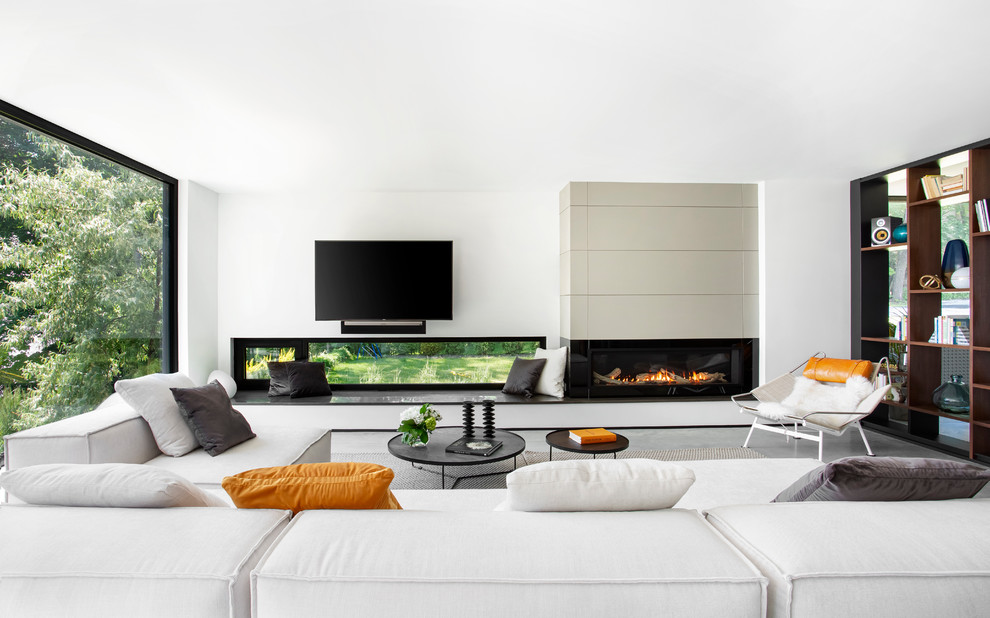 Modelo de sala de estar abierta moderna grande con paredes blancas, suelo de cemento, todas las chimeneas, marco de chimenea de piedra, televisor colgado en la pared y suelo gris