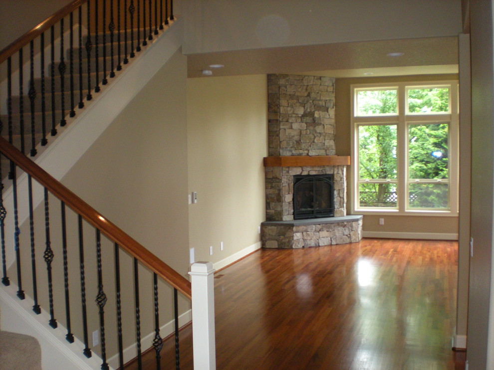 Foto de sala de estar cerrada tradicional de tamaño medio con paredes beige, suelo de madera en tonos medios, chimenea de esquina, marco de chimenea de piedra y suelo marrón
