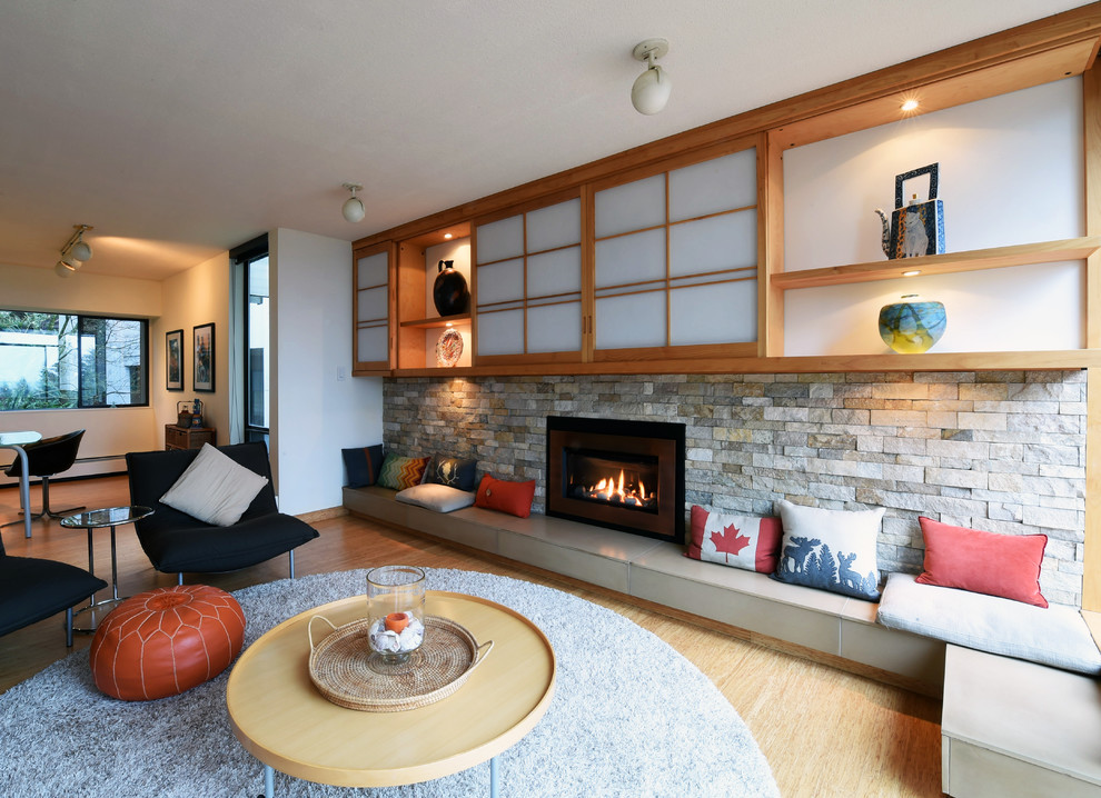 Example of a mid-sized trendy enclosed bamboo floor and beige floor family room design in Vancouver with white walls, a standard fireplace, a stone fireplace and a media wall