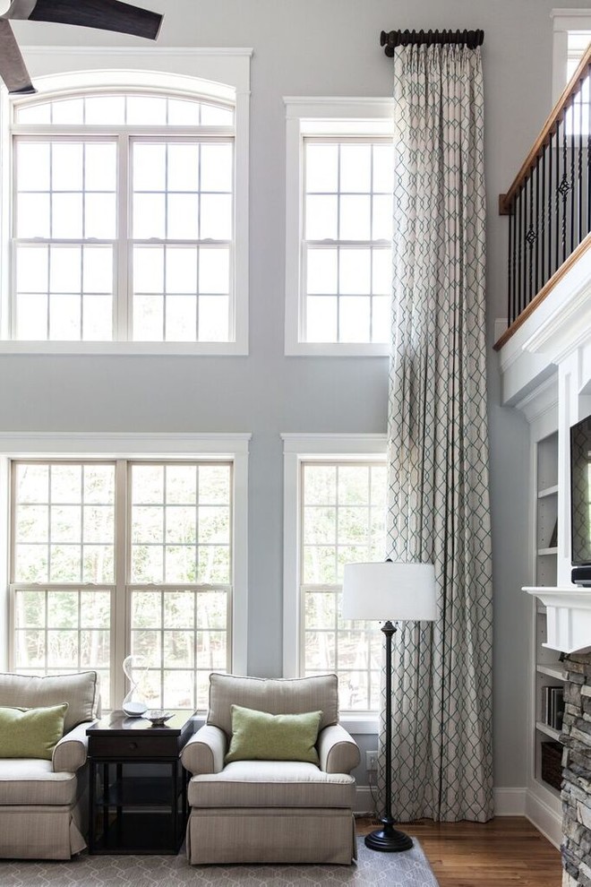 Modelo de sala de estar abierta clásica renovada grande con paredes grises, suelo de madera en tonos medios, todas las chimeneas, marco de chimenea de piedra y televisor colgado en la pared