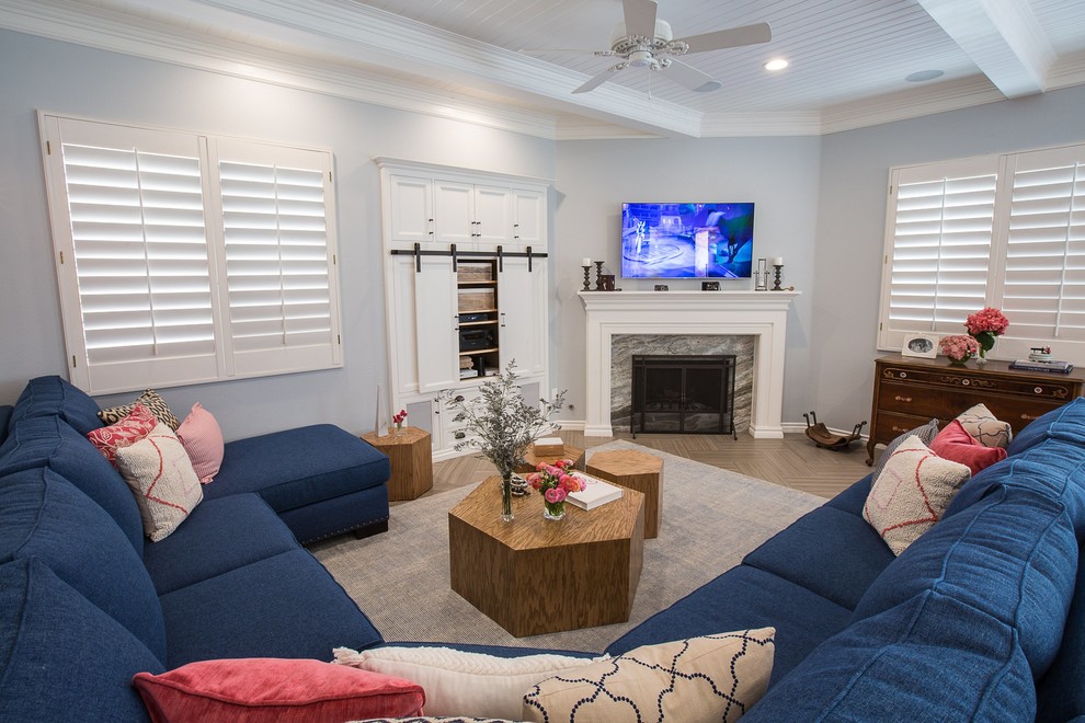 Пример оригинального дизайна: большая открытая гостиная комната в стиле неоклассика (современная классика) с синими стенами, полом из керамической плитки, угловым камином, фасадом камина из дерева, телевизором на стене и коричневым полом