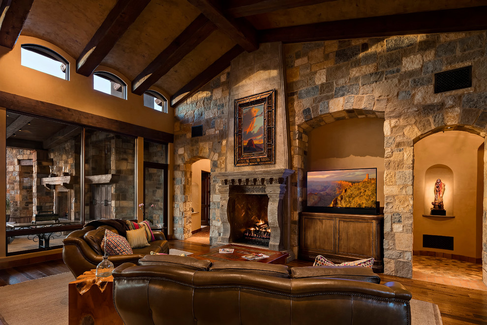 Cette image montre une salle de séjour sud-ouest américain fermée avec un sol en bois brun, une cheminée standard, un manteau de cheminée en pierre, un mur beige et un téléviseur encastré.