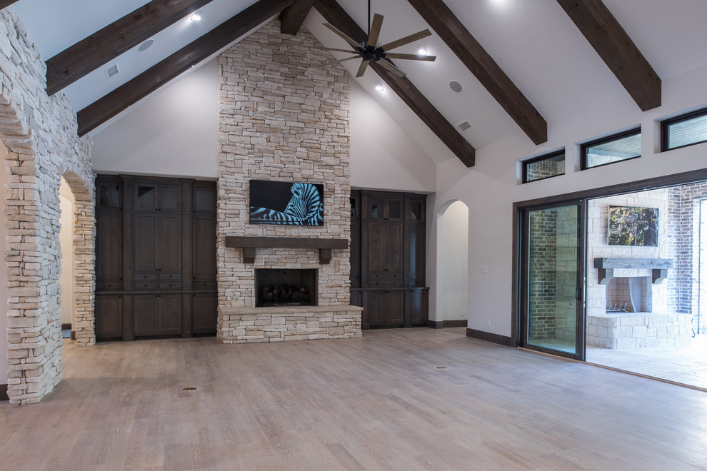 Design ideas for a large classic open plan games room in Dallas with white walls, medium hardwood flooring, a standard fireplace, a stone fireplace surround, a wall mounted tv and brown floors.