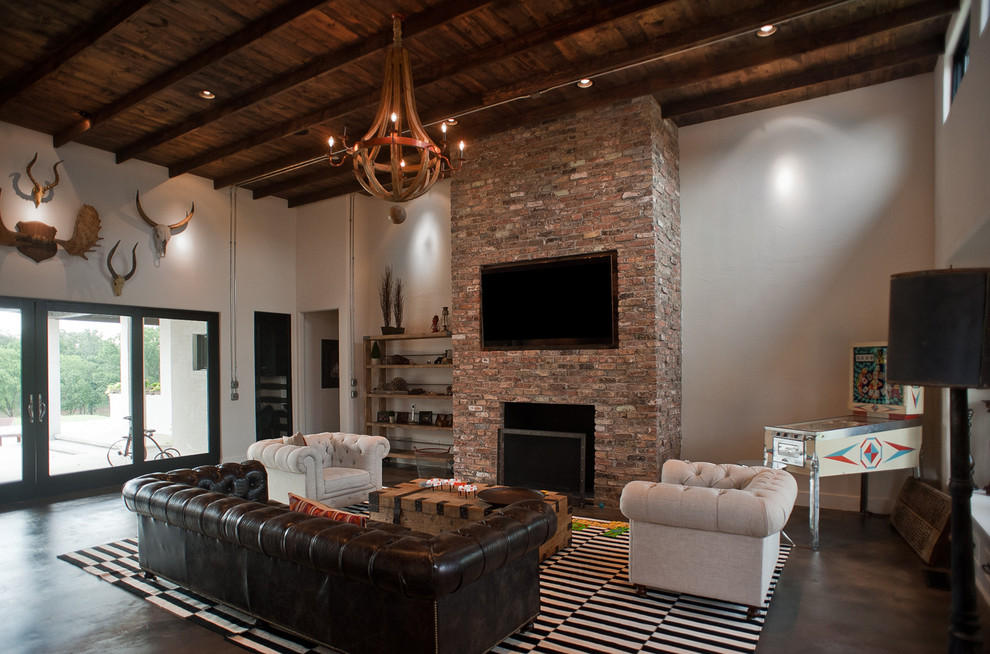 This is an example of a large rustic open plan games room in Oklahoma City with white walls, concrete flooring, a standard fireplace, a brick fireplace surround and a wall mounted tv.