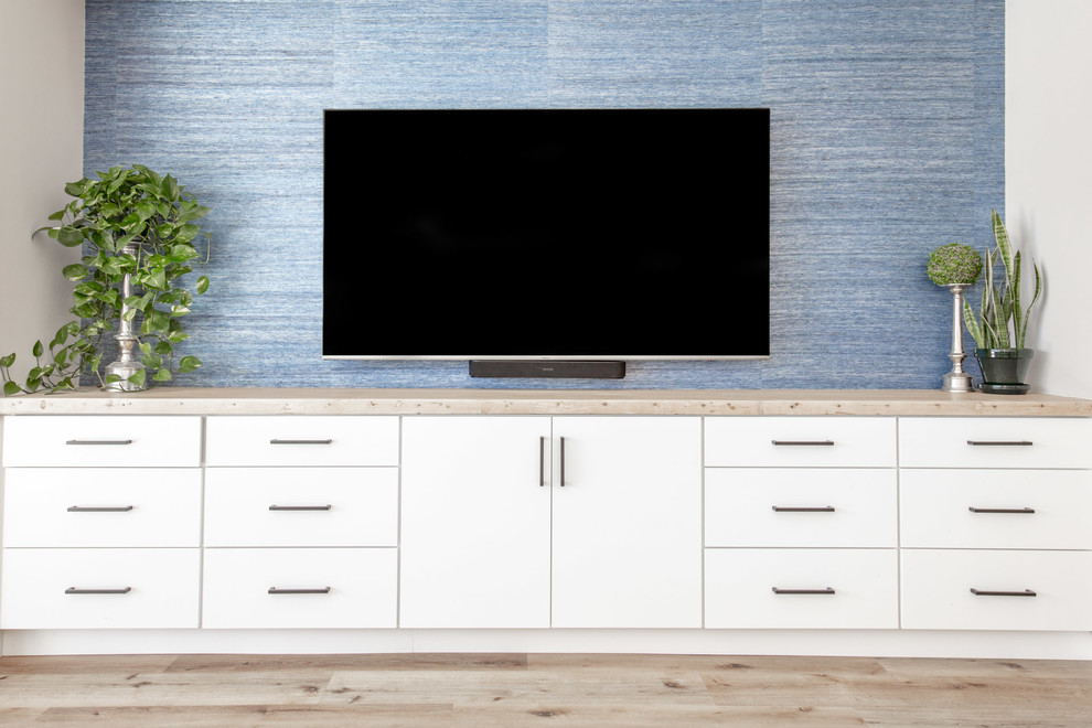Diseño de sala de estar abierta contemporánea grande sin chimenea con paredes azules, suelo de madera clara, televisor colgado en la pared y suelo beige