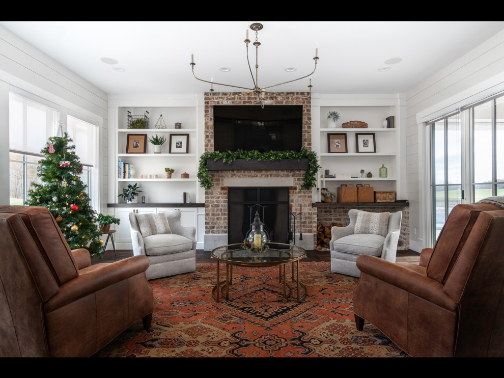 This is an example of a medium sized country enclosed games room in Other with white walls, dark hardwood flooring, a standard fireplace, a brick fireplace surround, a wall mounted tv and brown floors.
