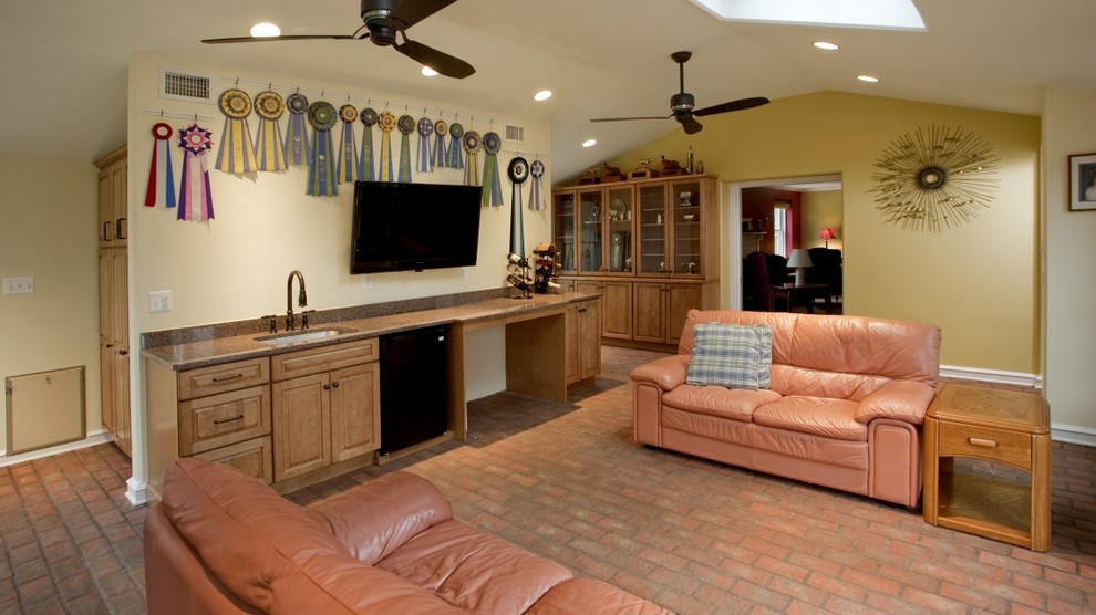 Modelo de sala de estar con barra de bar cerrada actual de tamaño medio con paredes amarillas, suelo de ladrillo, televisor colgado en la pared y suelo marrón