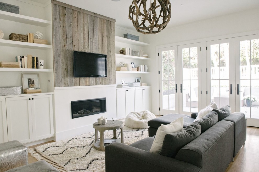 Ejemplo de sala de estar con biblioteca costera con paredes blancas, chimenea lineal, televisor colgado en la pared y alfombra