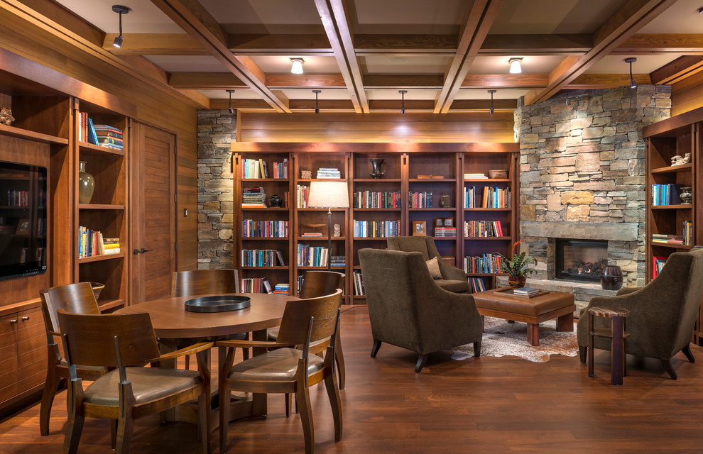 Exemple d'une salle de séjour montagne fermée avec une bibliothèque ou un coin lecture, un sol en bois brun, une cheminée standard, un manteau de cheminée en pierre et un téléviseur fixé au mur.