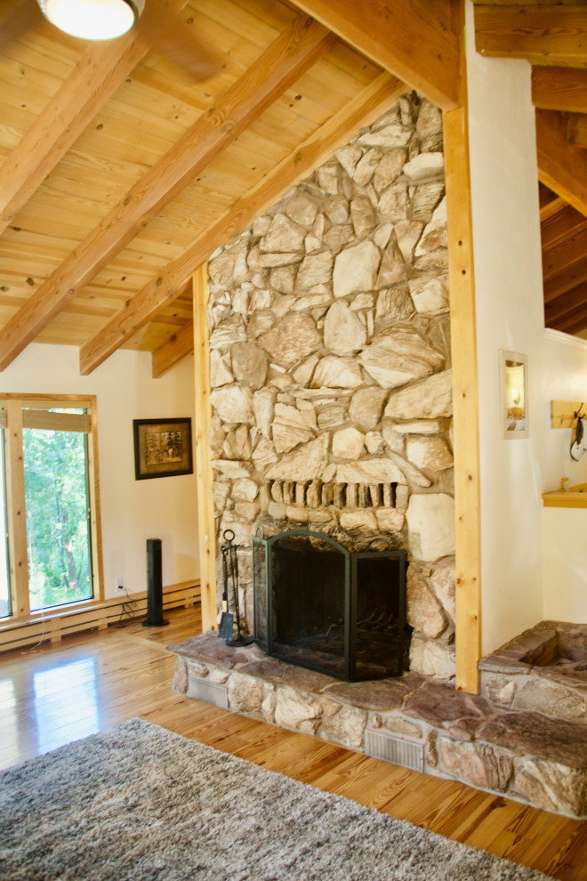 This is an example of a medium sized rustic open plan games room in Other with beige walls, light hardwood flooring, a standard fireplace, a stone fireplace surround, a freestanding tv, brown floors and a vaulted ceiling.