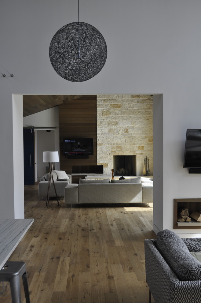 На фото: открытая гостиная комната в стиле модернизм с коричневыми стенами, светлым паркетным полом, стандартным камином, фасадом камина из камня и телевизором на стене