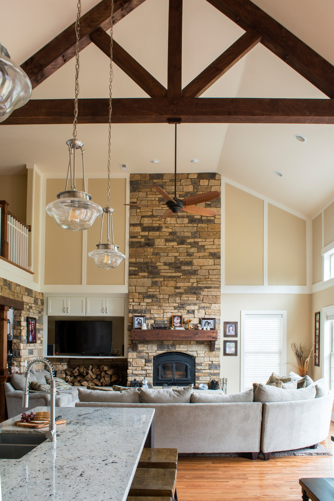 Example of a large mountain style open concept light wood floor family room design in Charlotte with beige walls, a standard fireplace, a stone fireplace and a media wall