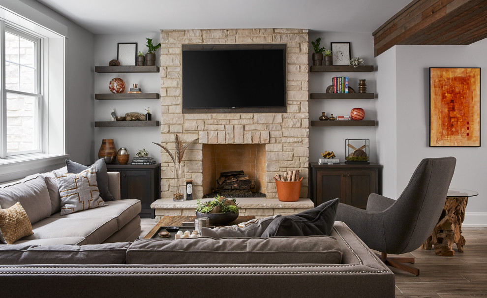 This is an example of a classic open plan games room in Chicago with grey walls, a standard fireplace, a stone fireplace surround, a wall mounted tv and brown floors.
