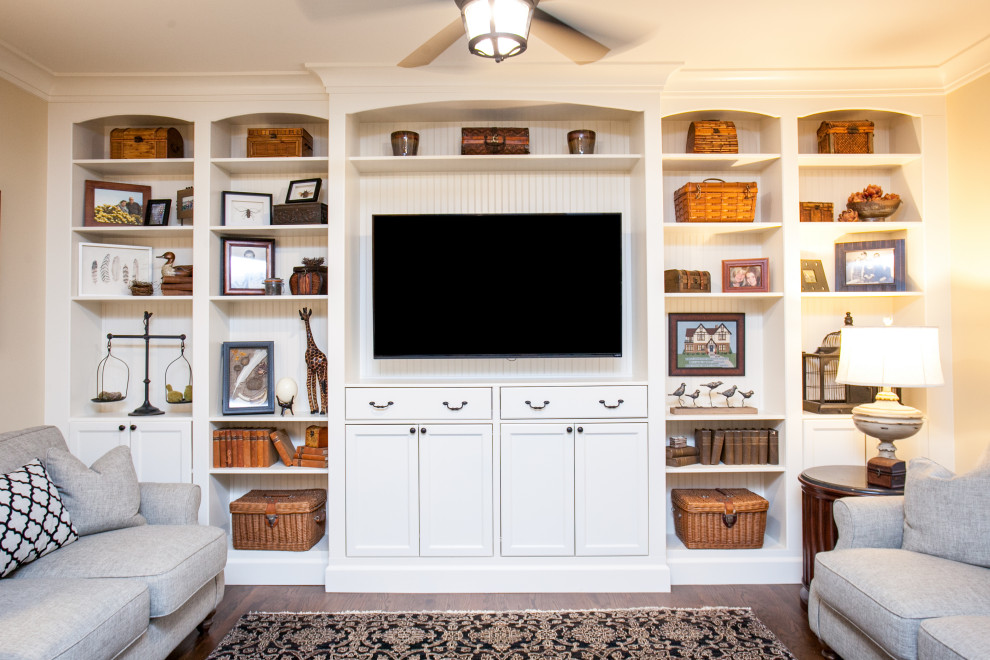 Modelo de sala de estar tradicional con paredes beige, suelo de madera oscura, pared multimedia y suelo marrón