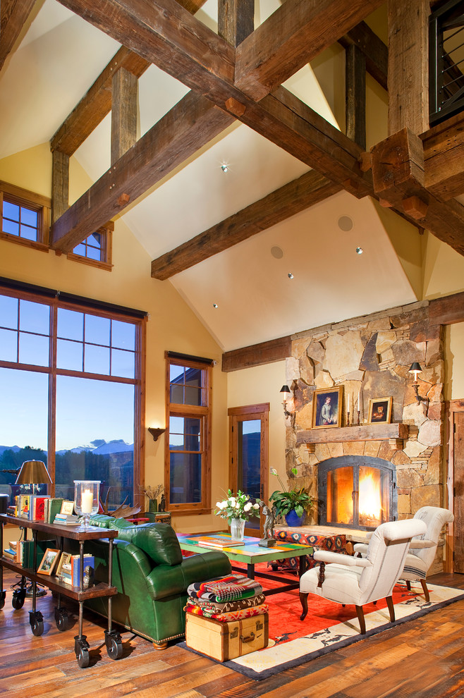 Idée de décoration pour une salle de séjour chalet ouverte avec un mur beige, un sol en bois brun, une cheminée standard et un manteau de cheminée en pierre.