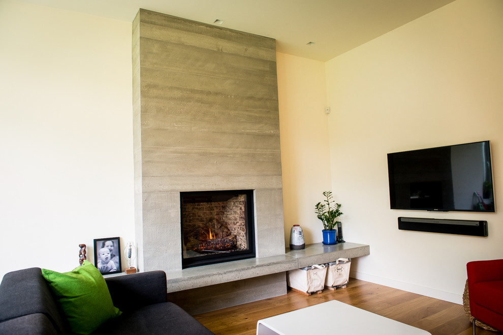 Exemple d'une grande salle de séjour moderne ouverte avec un mur blanc, un sol en bois brun, une cheminée standard, un manteau de cheminée en béton et un téléviseur fixé au mur.