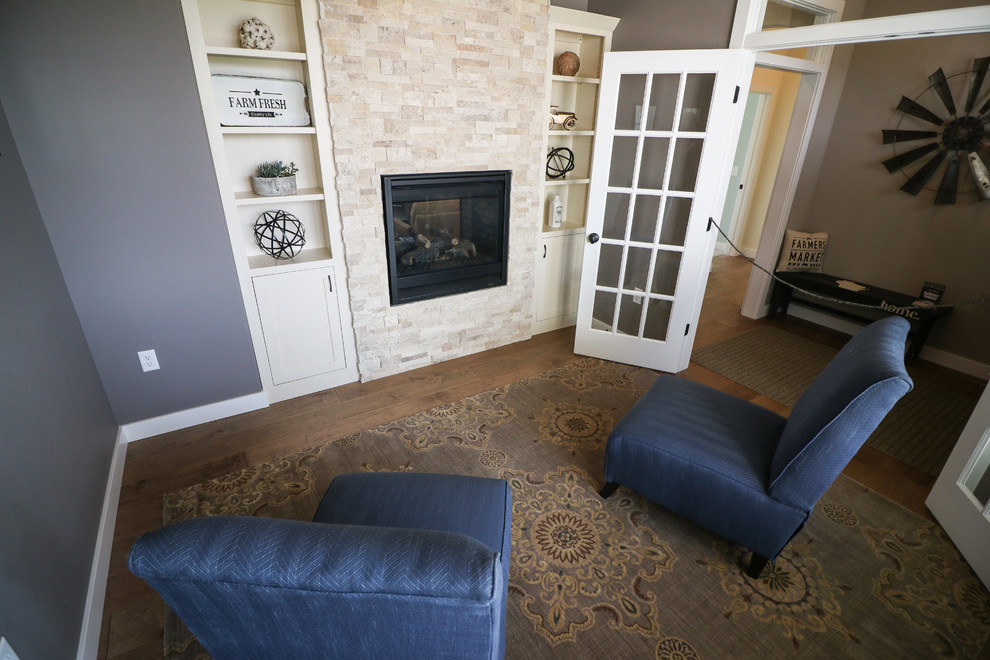 Cette photo montre une salle de séjour éclectique de taille moyenne et fermée avec un mur gris, un sol en bois brun, une cheminée double-face, un manteau de cheminée en pierre, aucun téléviseur et un sol marron.
