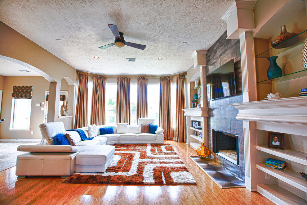 Example of a large trendy open concept light wood floor family room design in Houston with beige walls, a standard fireplace and a tile fireplace
