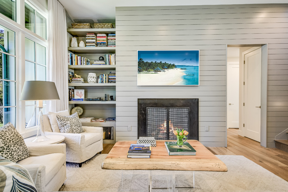 Пример оригинального дизайна: открытая гостиная комната в морском стиле с с книжными шкафами и полками, серыми стенами, стандартным камином, телевизором на стене и светлым паркетным полом