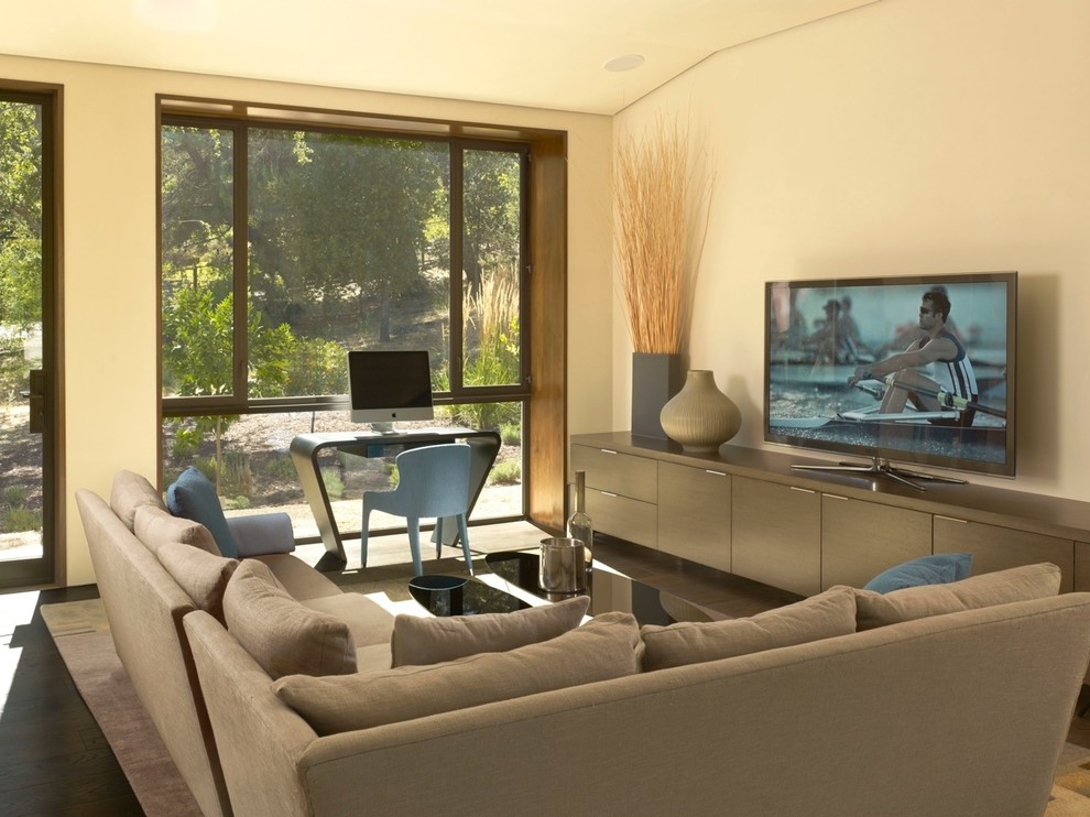 Diseño de sala de estar actual con paredes beige, suelo de madera oscura y televisor independiente
