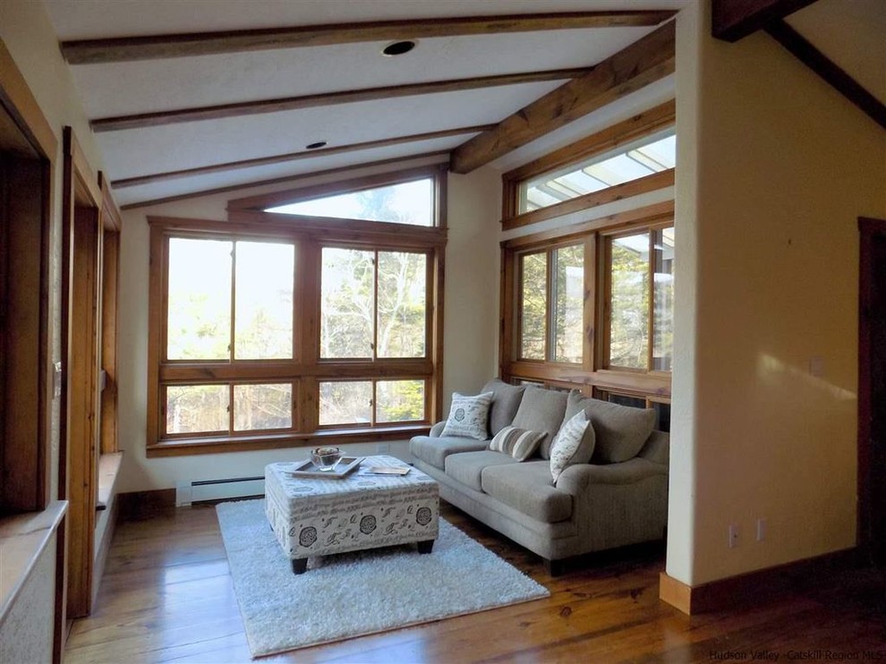 Diseño de sala de estar abierta de estilo americano pequeña con paredes beige, suelo de madera en tonos medios y pared multimedia