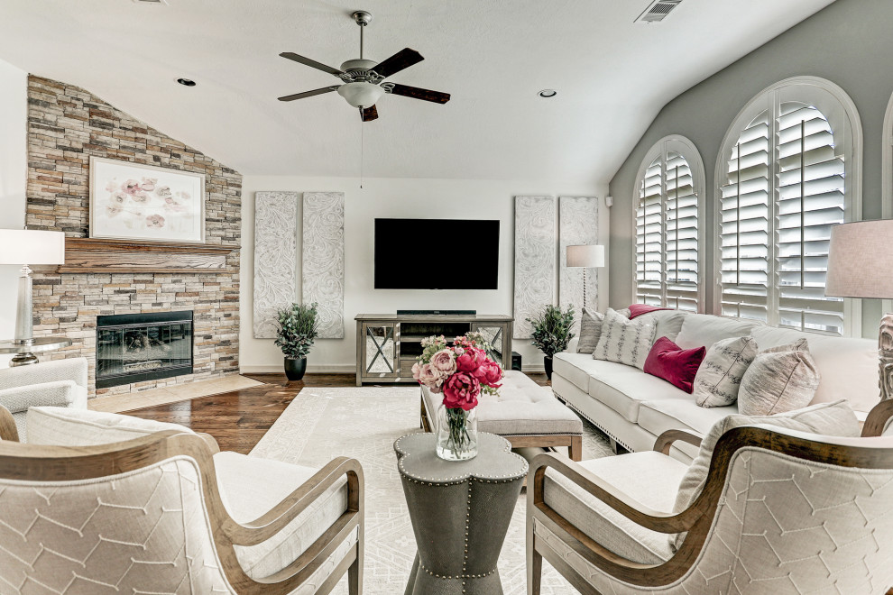 Example of a mid-sized transitional brown floor, vaulted ceiling and dark wood floor family room design in Houston with white walls, a corner fireplace, a stone fireplace and a wall-mounted tv
