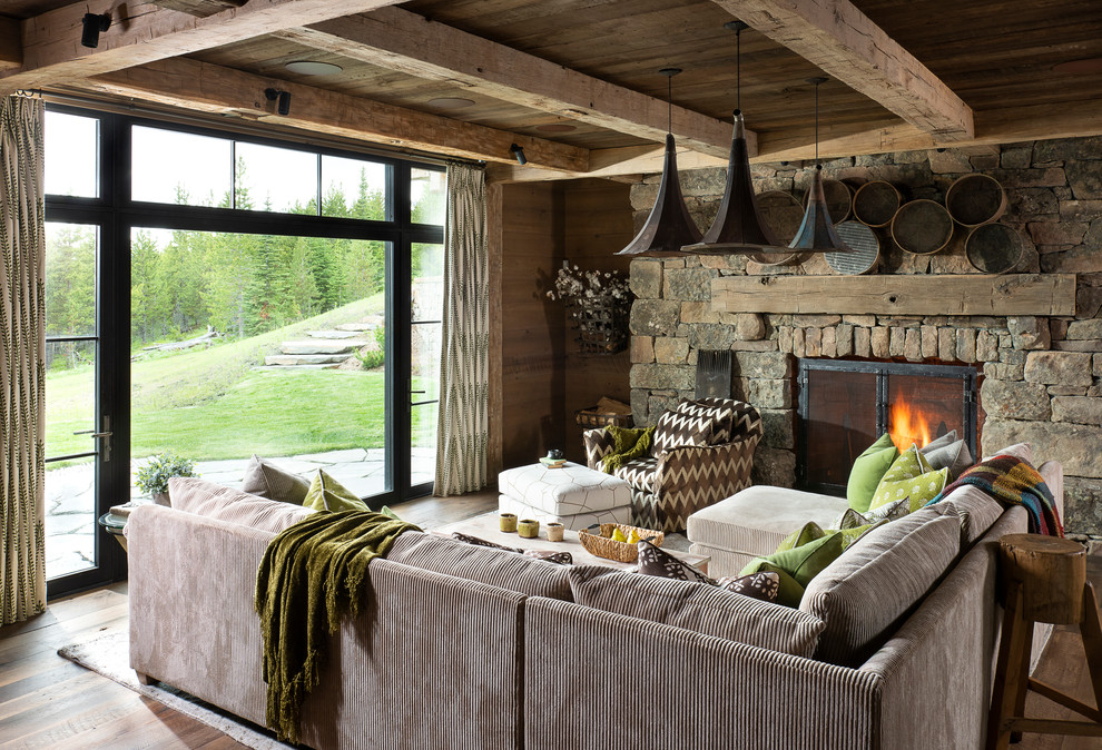 Imagen de sala de estar abierta rural grande con paredes marrones, suelo de madera en tonos medios, todas las chimeneas, marco de chimenea de piedra y suelo marrón