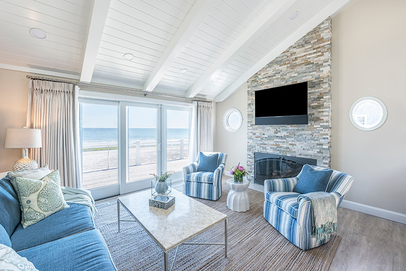 На фото: открытая гостиная комната среднего размера в морском стиле с бежевыми стенами, стандартным камином, фасадом камина из камня, телевизором на стене, светлым паркетным полом, бежевым полом и ковром на полу