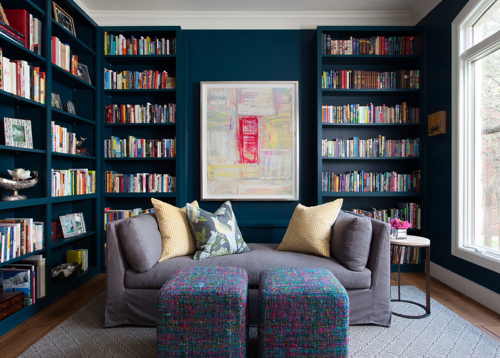 Cette image montre une salle de séjour traditionnelle avec une bibliothèque ou un coin lecture, un mur bleu et un sol en bois brun.