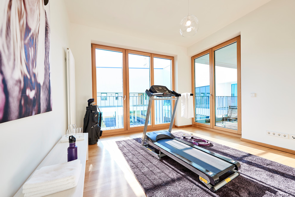 Medium sized contemporary home gym in Hamburg with white walls, medium hardwood flooring and brown floors.