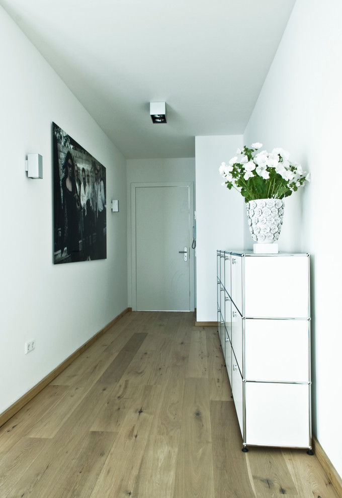 Idée de décoration pour un couloir design de taille moyenne avec un sol en bois brun et un mur blanc.
