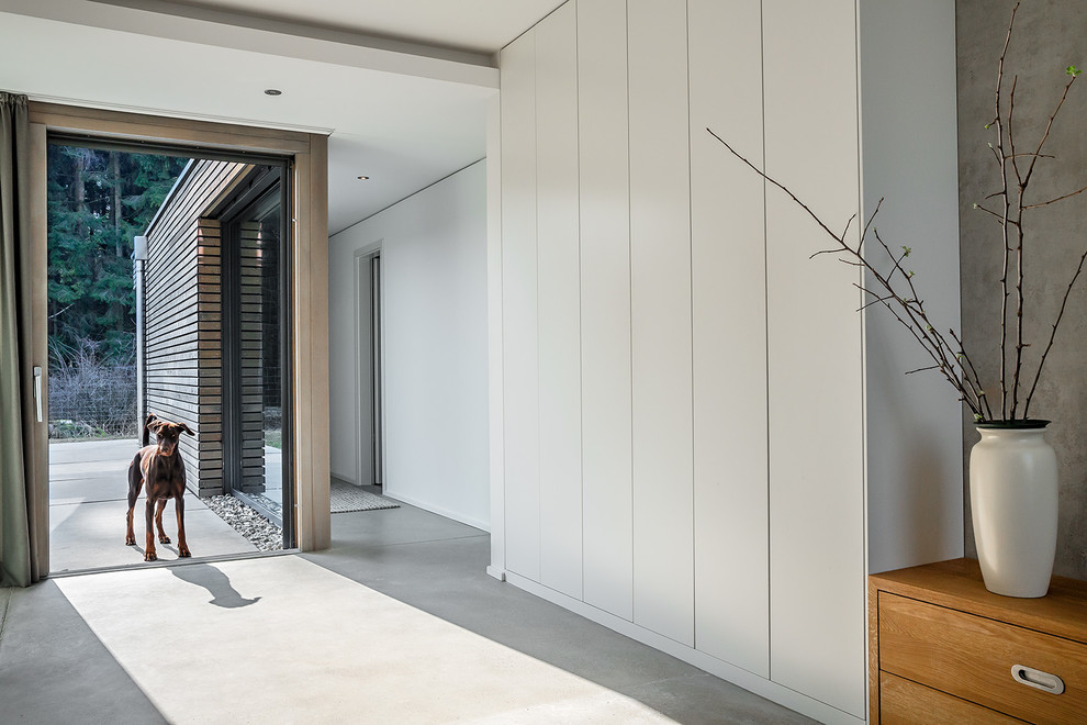 Idée de décoration pour un grand couloir design avec un mur blanc, sol en béton ciré et un sol gris.