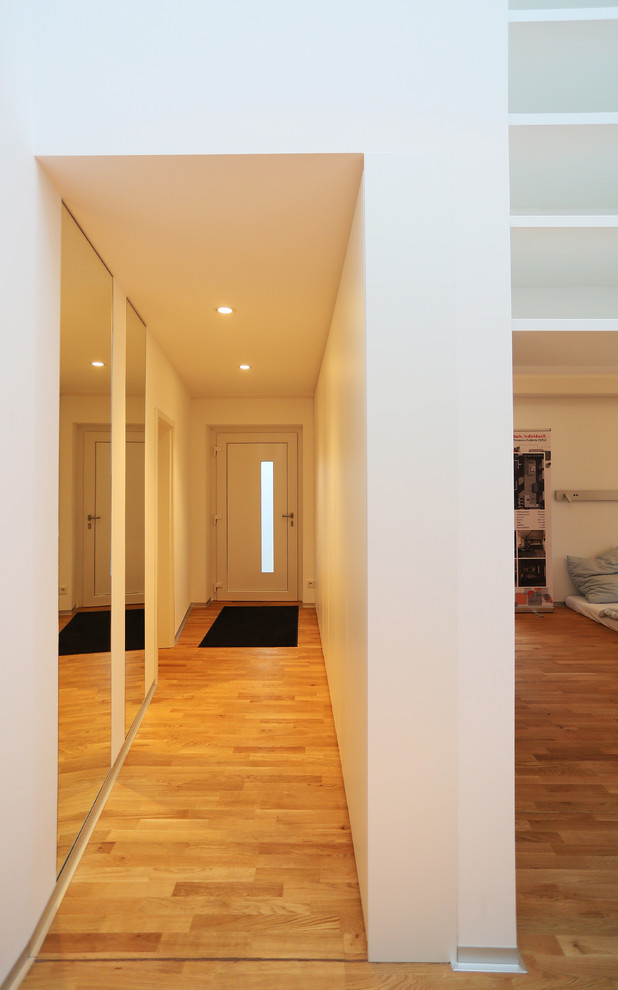 Geräumiger Moderner Flur mit weißer Wandfarbe, hellem Holzboden und braunem Boden in Berlin