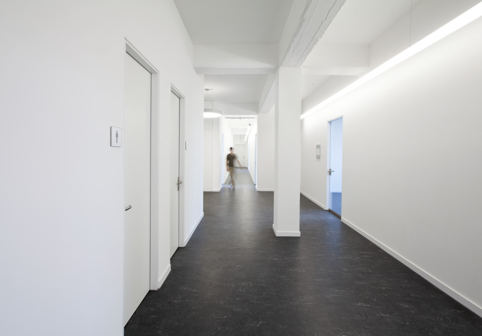 Cette image montre un couloir design avec un mur blanc et un sol noir.