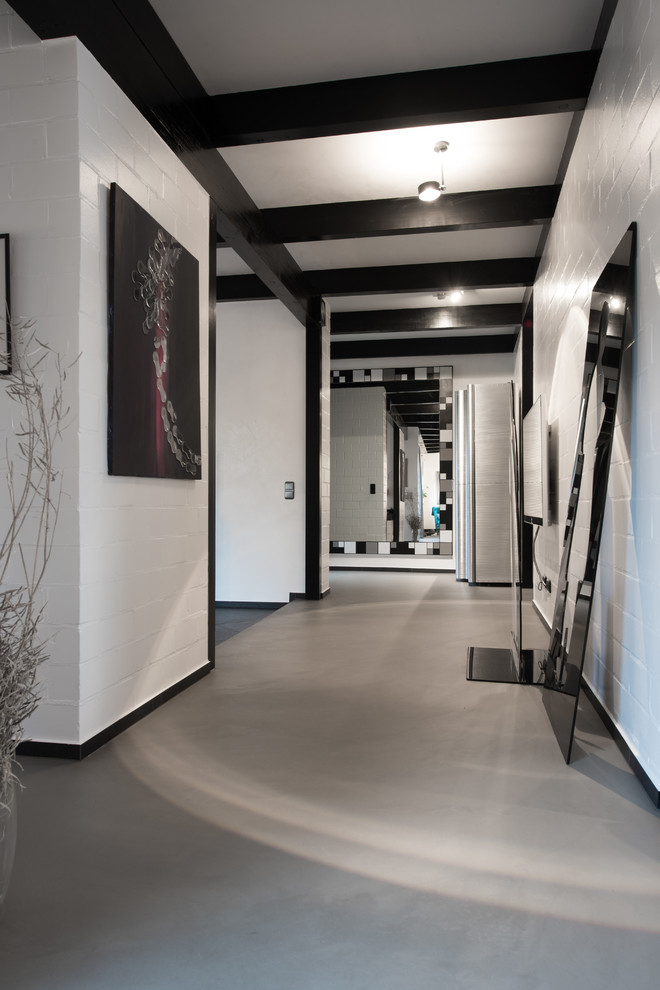 Стильный дизайн: большой коридор: освещение в современном стиле с белыми стенами, бетонным полом и серым полом - последний тренд
