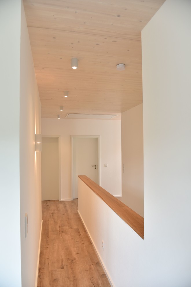 Idée de décoration pour un couloir design avec un mur blanc, sol en stratifié et un sol marron.