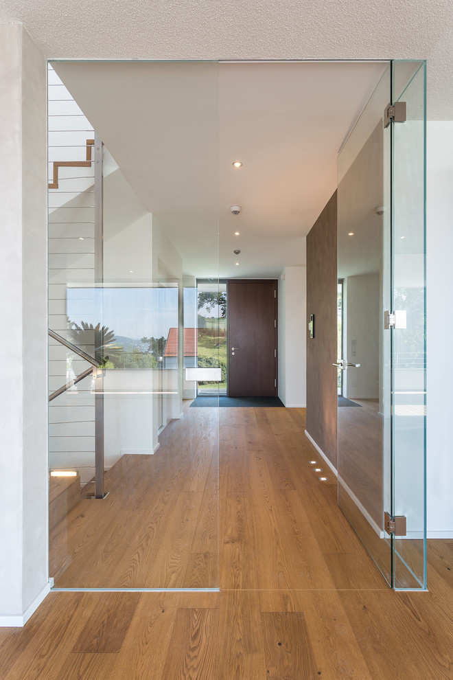 Idée de décoration pour un grand couloir design avec un mur blanc et un sol en bois brun.