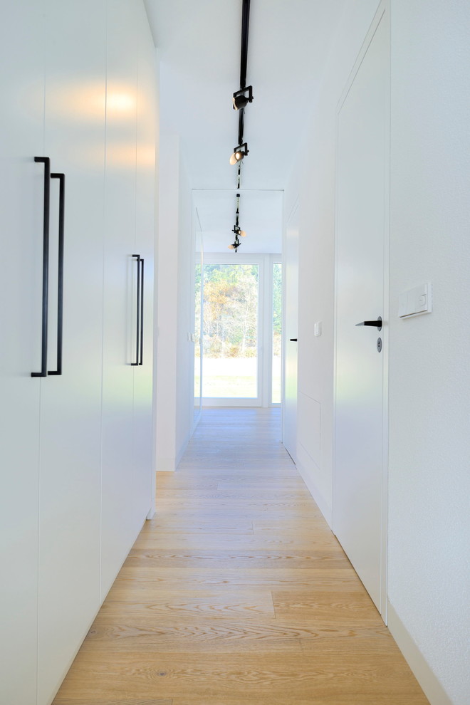 Inspiration pour un couloir minimaliste de taille moyenne avec un mur blanc et parquet clair.