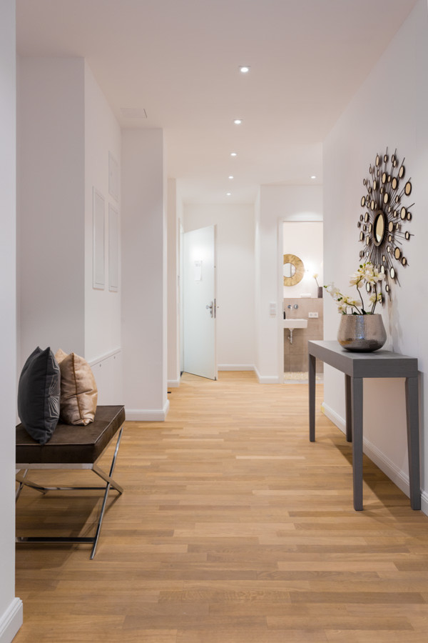 Cette image montre un couloir design de taille moyenne avec un mur blanc, un sol en bois brun et un sol marron.