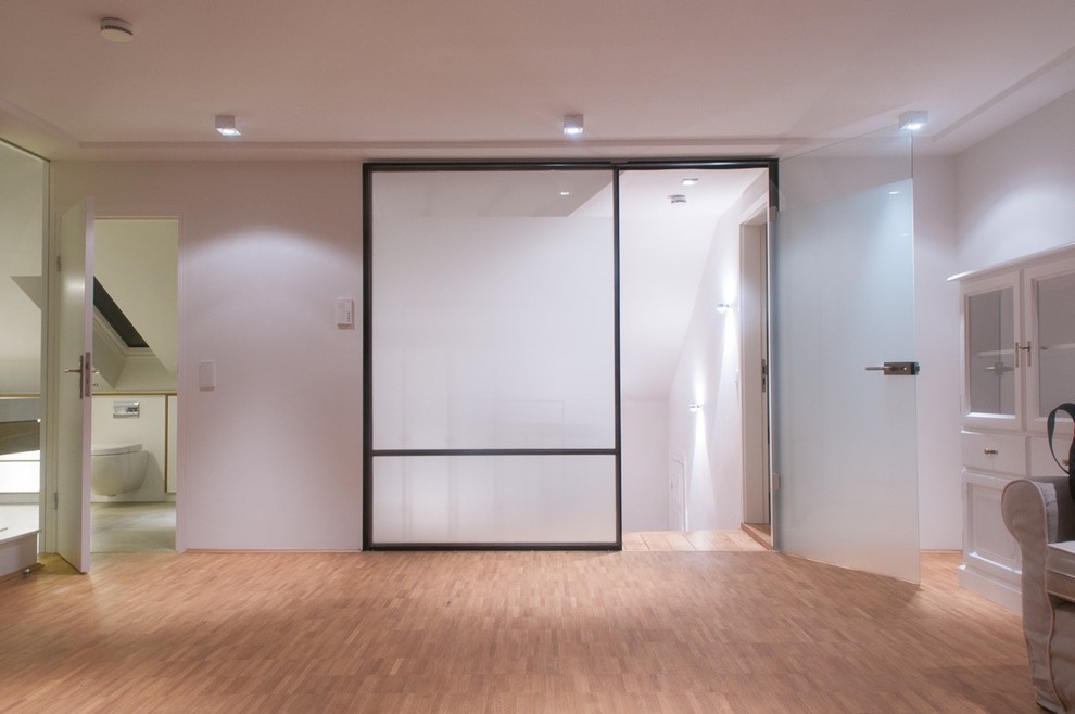 Cette photo montre un grand couloir chic avec un mur blanc et un sol en bois brun.