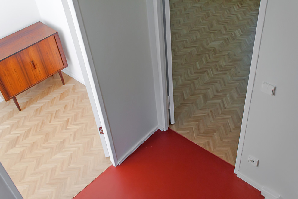 Cette image montre un couloir minimaliste avec un sol en linoléum, un mur blanc et un sol rouge.