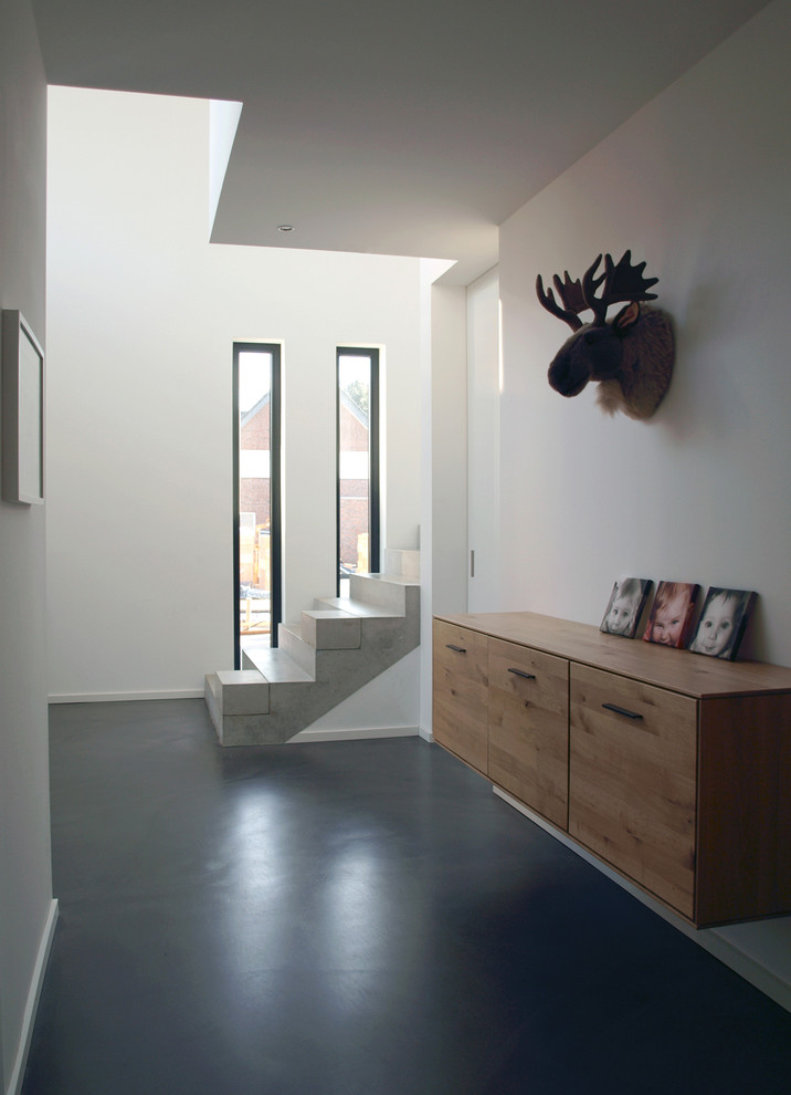 Aménagement d'un couloir moderne avec un mur blanc, sol en béton ciré et un sol noir.