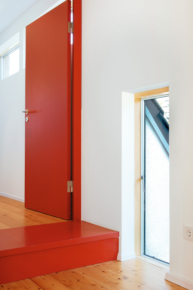 Immagine di un ingresso o corridoio design di medie dimensioni con pareti bianche, parquet chiaro e pavimento rosso