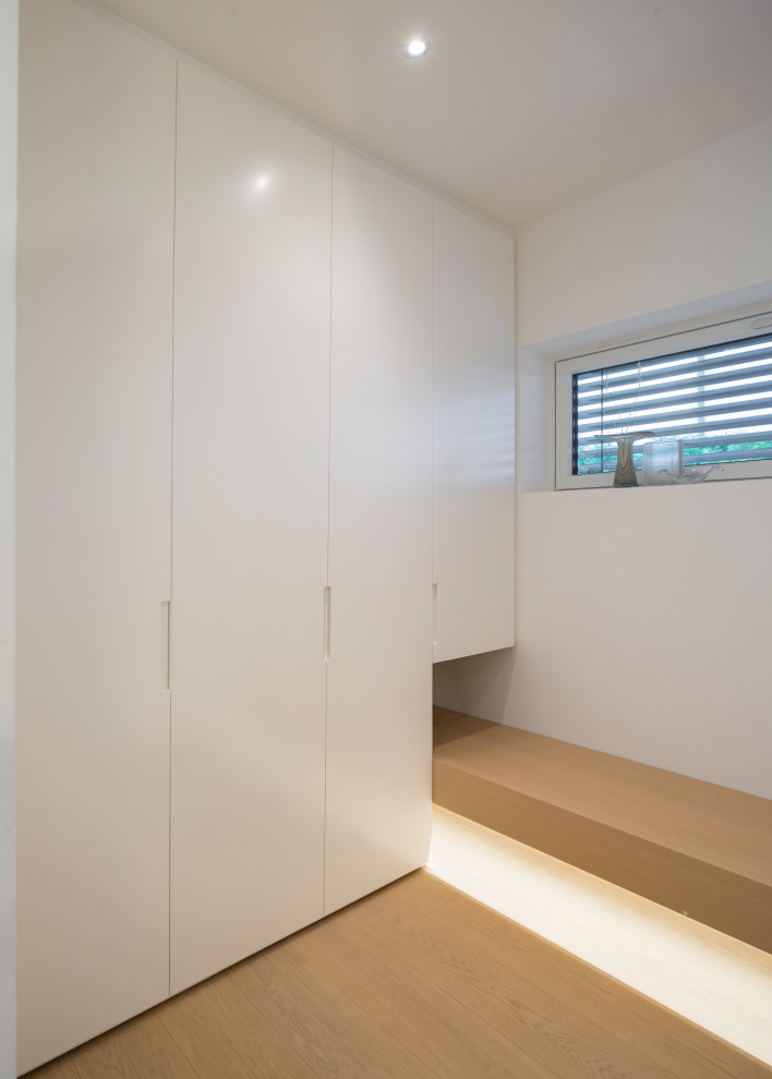 На фото: встроенный шкаф в стиле модернизм с плоскими фасадами, белыми фасадами и светлым паркетным полом