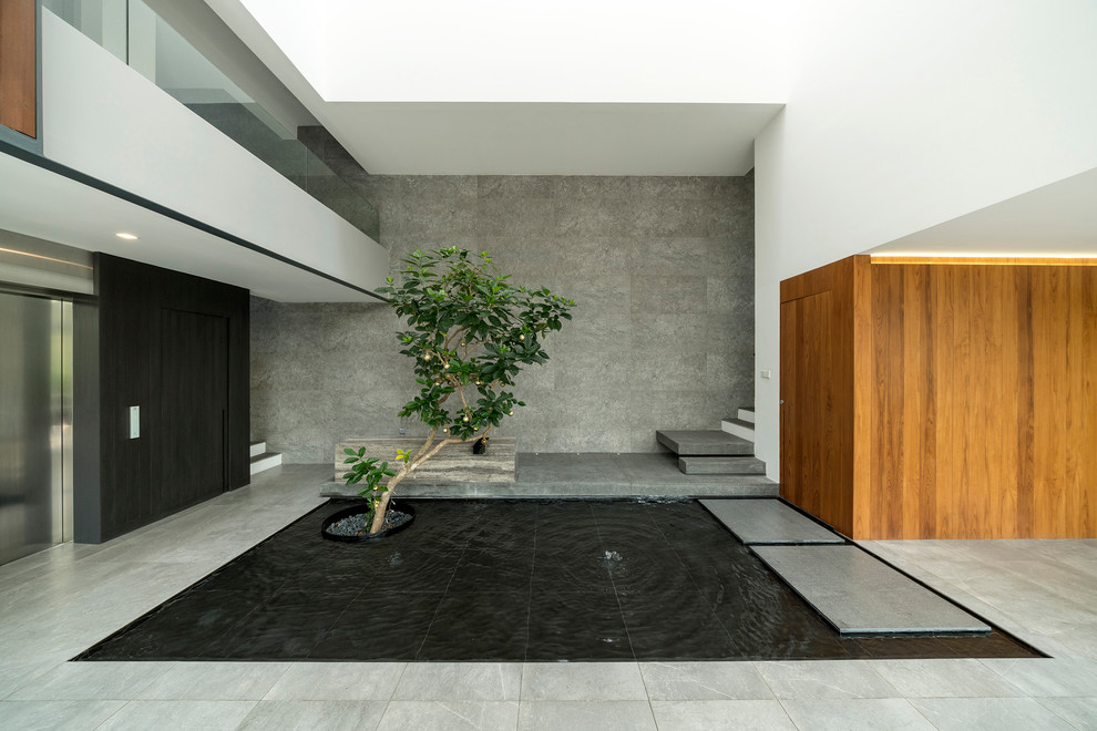 Cette image montre un hall d'entrée minimaliste avec un mur gris, une porte noire et un sol gris.