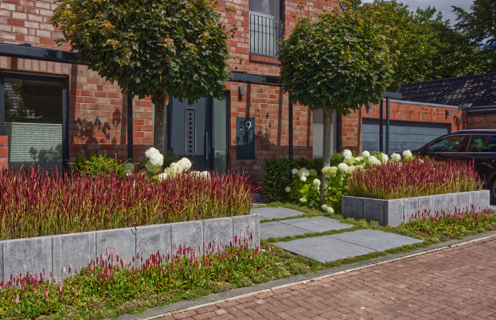 Aménagement d'un grand jardin avant contemporain l'été avec une exposition partiellement ombragée et des pavés en béton.