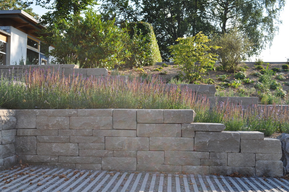 Idée de décoration pour un grand jardin arrière design l'automne avec un mur de soutènement, une exposition ombragée et des pavés en pierre naturelle.
